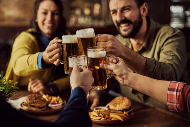 Close-up of group of friends toasting with beer while eating in a pub.
