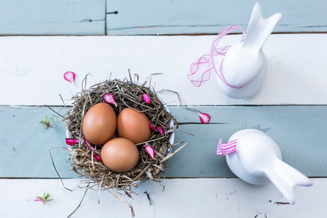 Nest of eggs with a striped background next to two white easter bunny ornaments. 