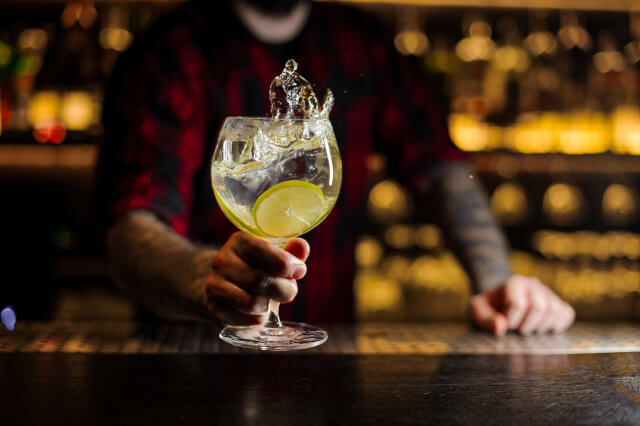 Mixologist holding a glass of fresh sour and sweet citrus cocktail.