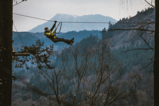 A man zip-lining with mountains in the background