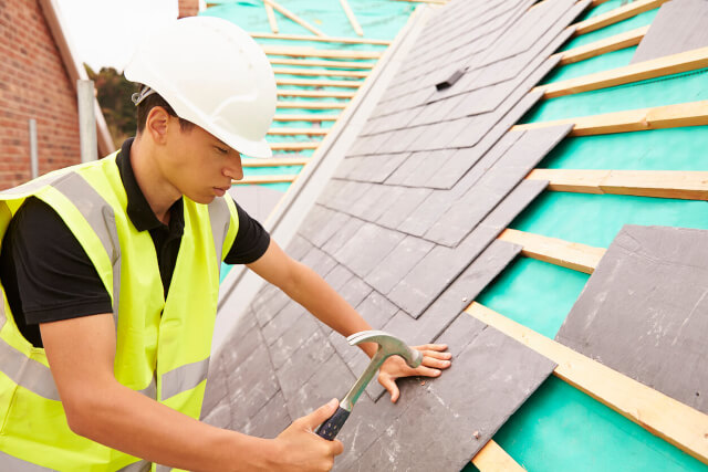 Builder with hammer repairing a roof.