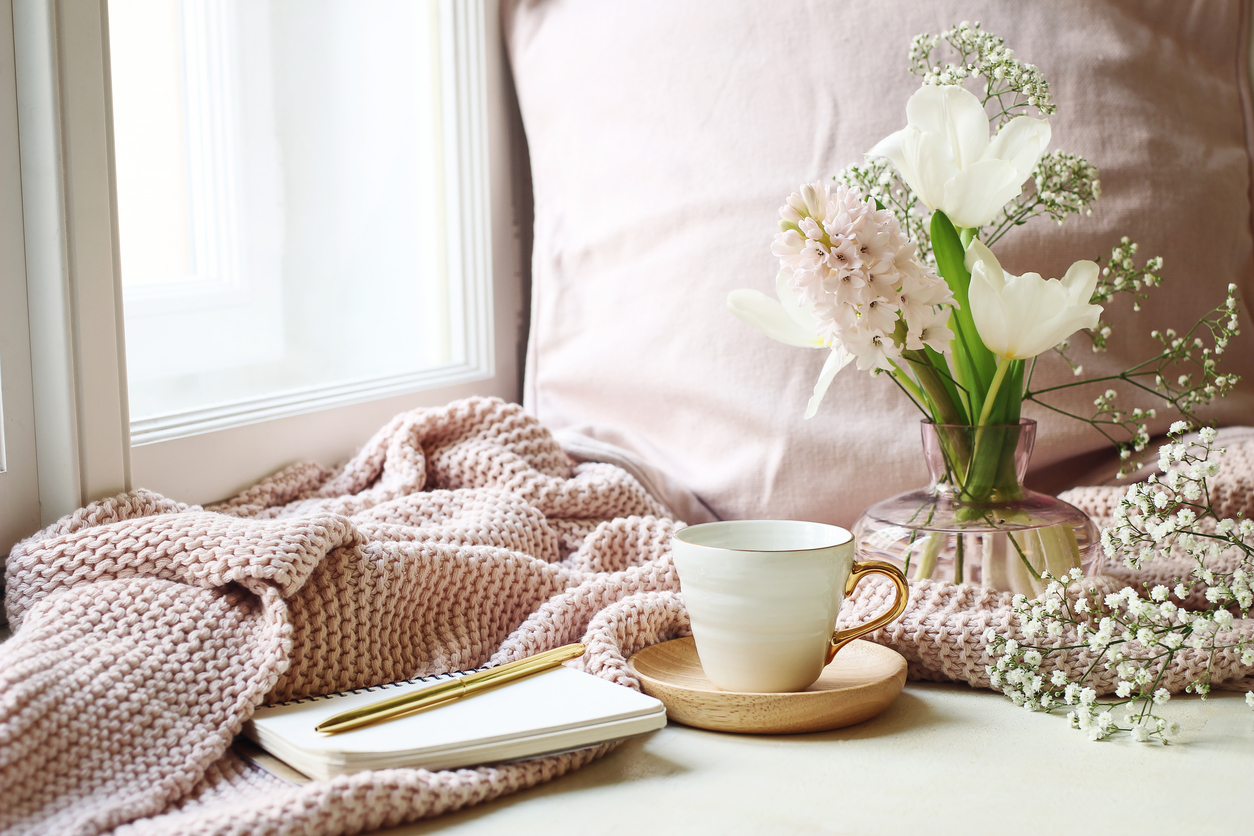 Cozy Easter, spring still life scene. Cup of coffee, opened notebook, pink knitted plaid on the windowsill. Vintage feminine styled photo, floral composition with tulips, hyacinth and Gypsophila flowers.