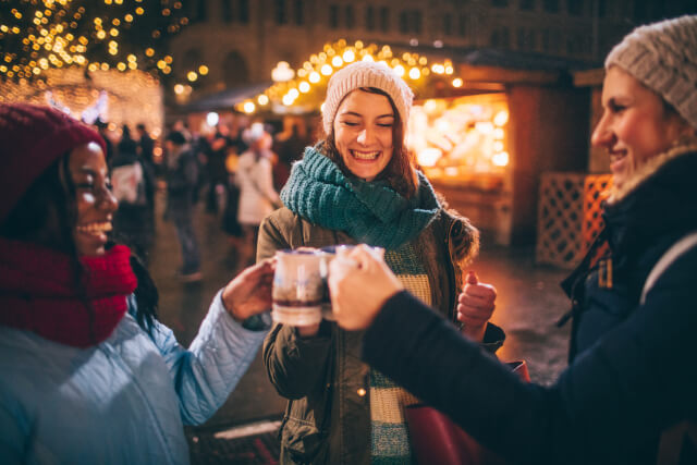 A group of three women toasting their drinks at a christmas market. 