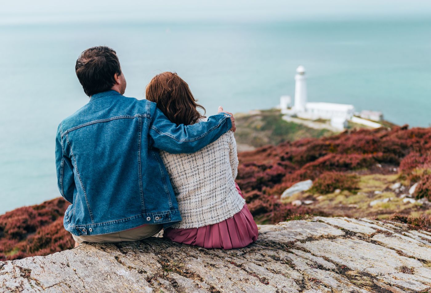 Couple sitting on a cliff, looking at South Stack Lighthouse in Anglesey
